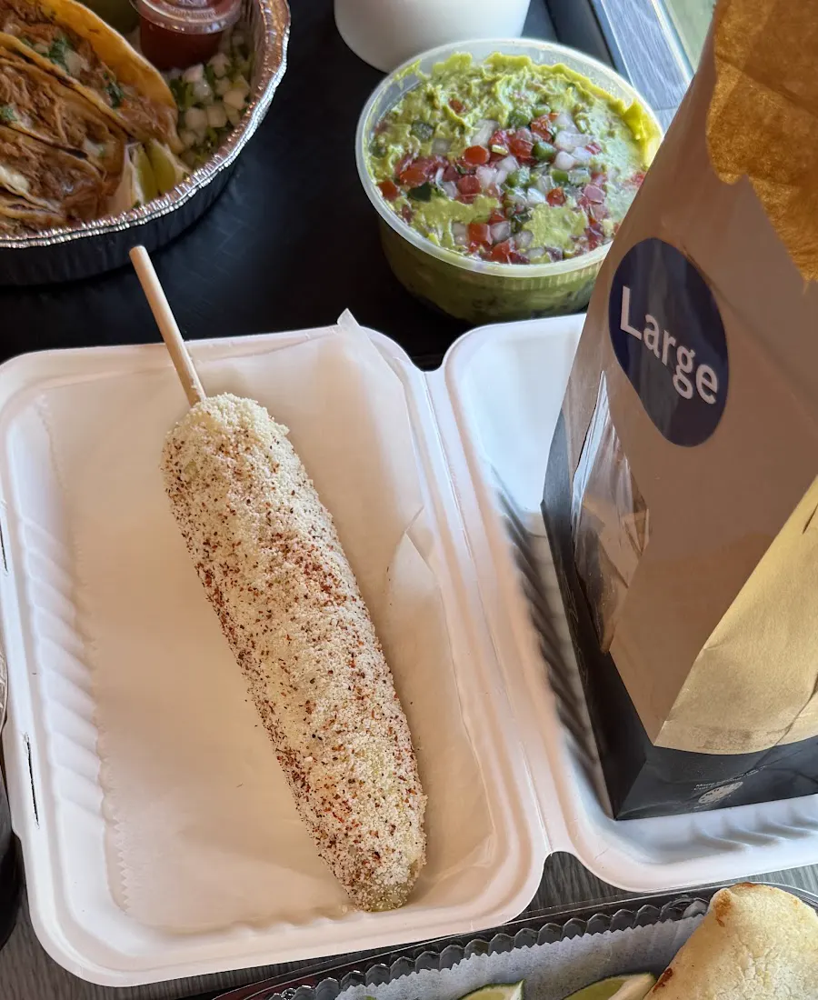 Elote dusted with cheese and chile, next to guacamole with pico de gallo