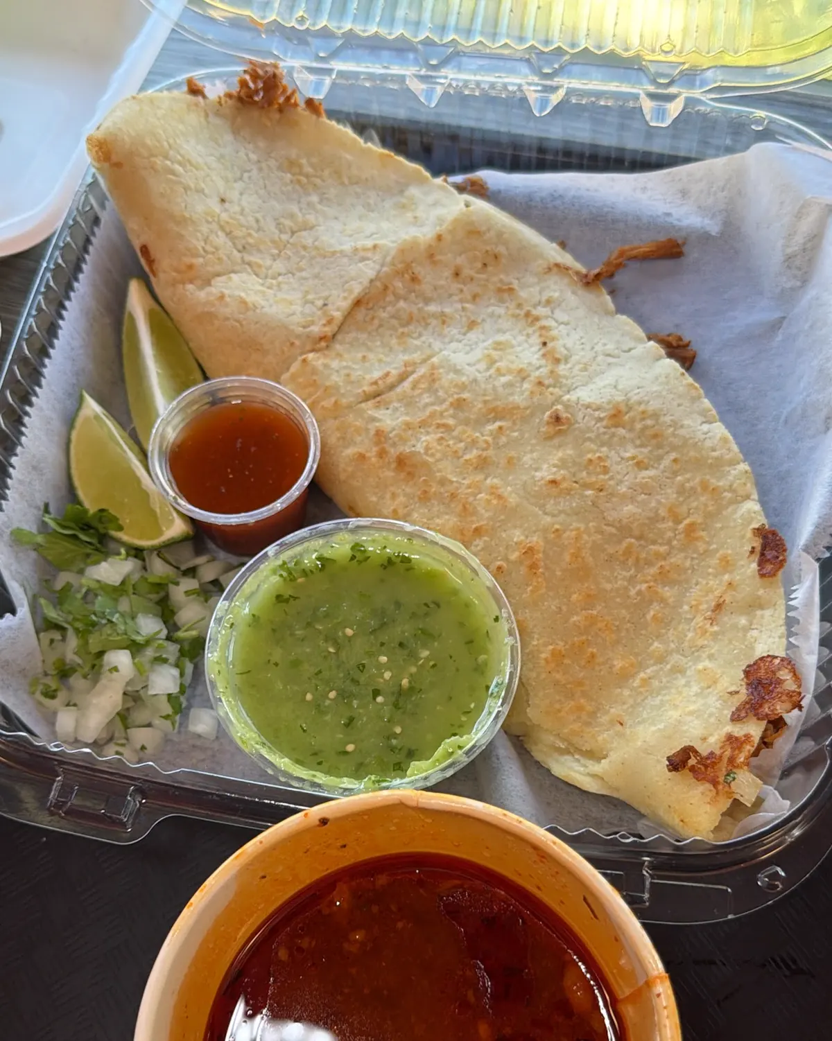 A quesabirria with salsa verde, red salsa, onion, cilantro, lime and a cup of consomé