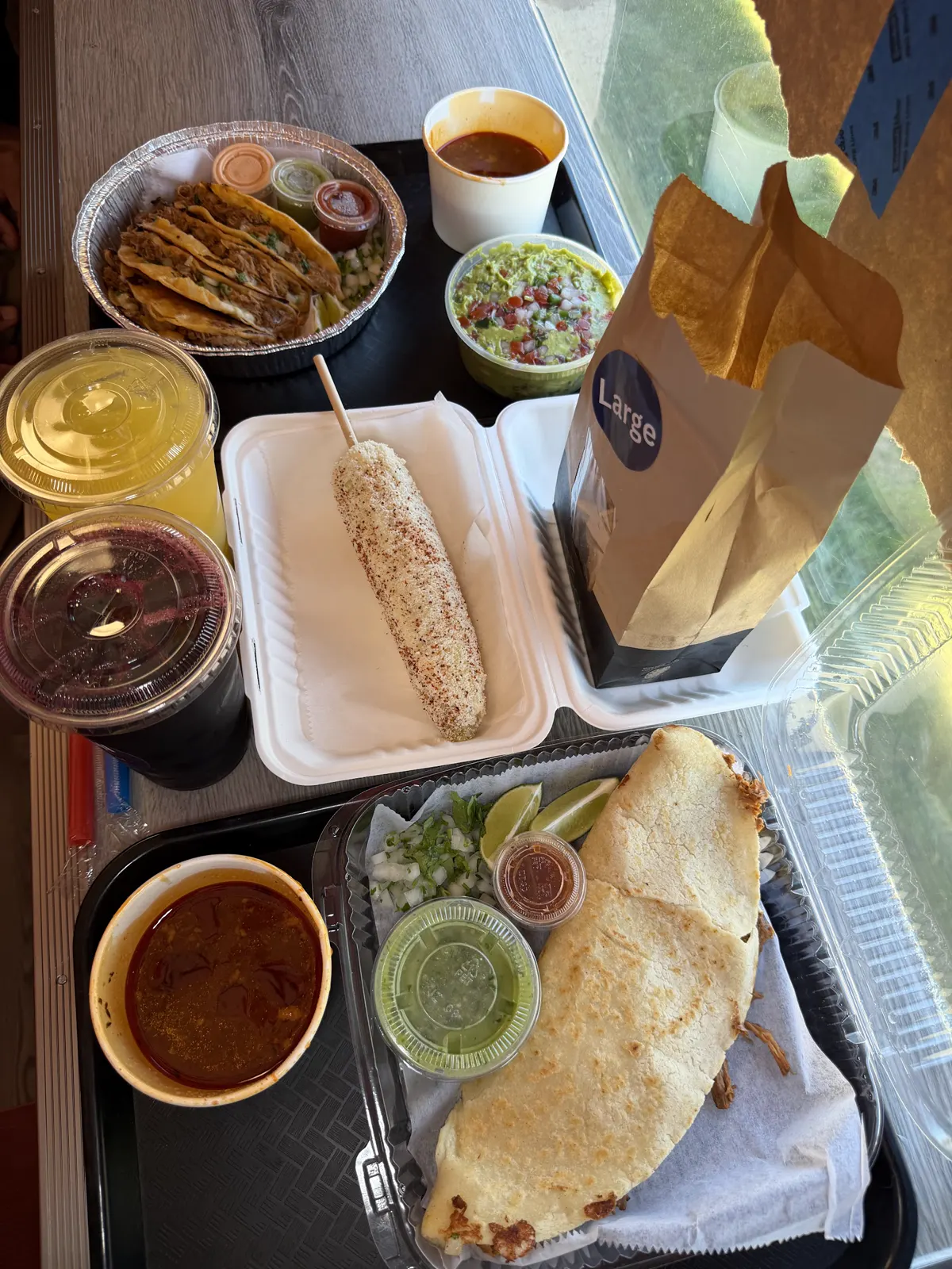 Birria tacos with consomé, quesabirria, elote, guacamole and two aguas frescas on a tray